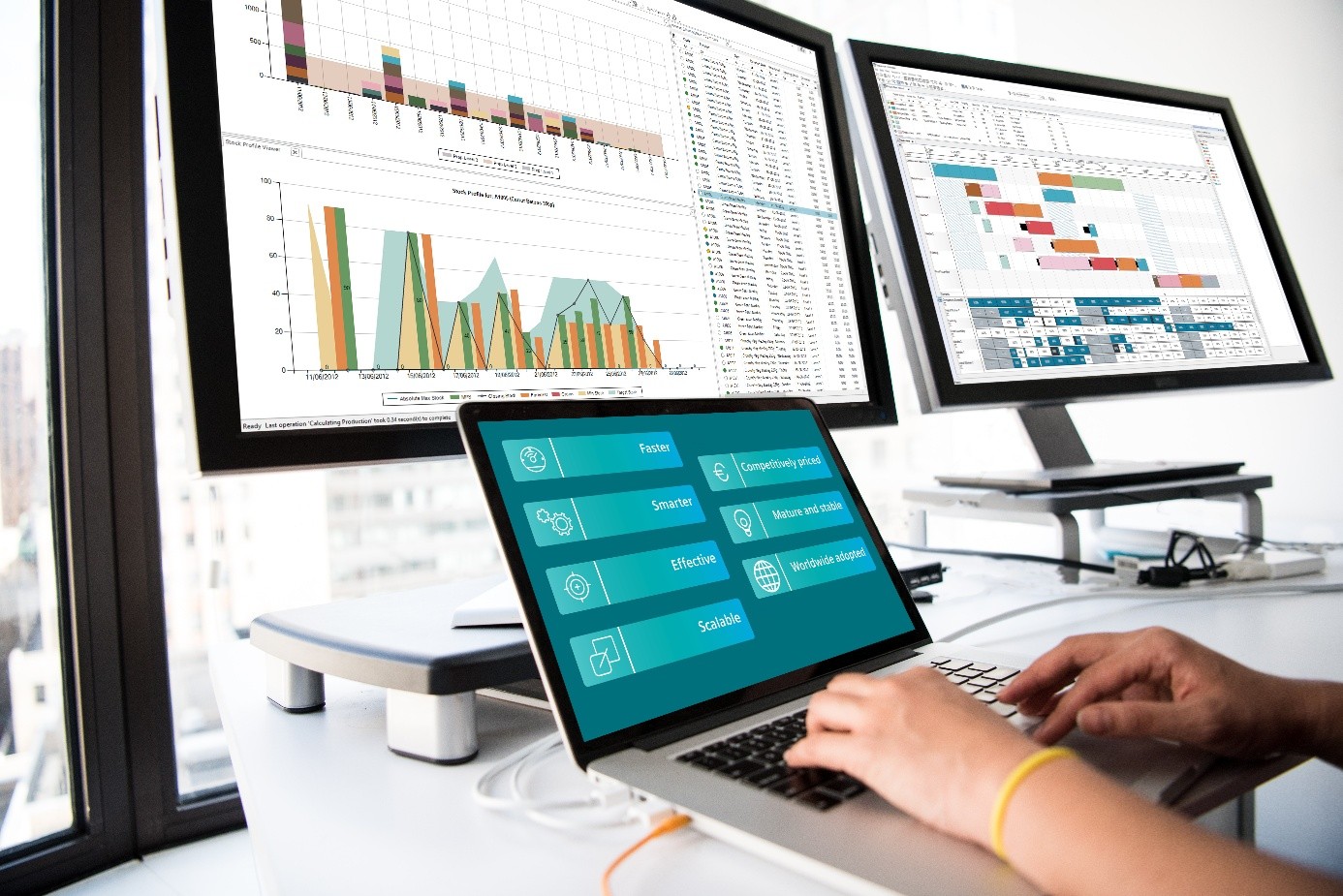 ilustrační obrázek - notebook s rukama a monitory s grafy